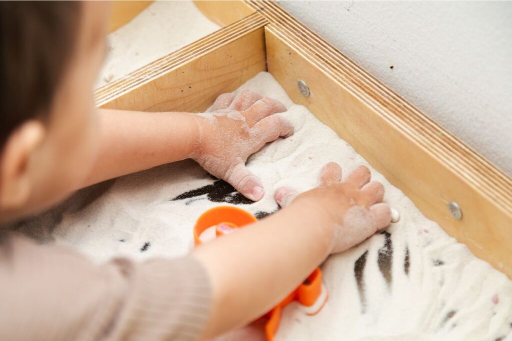 a child's hands exploring the sand and toys in a sensory table